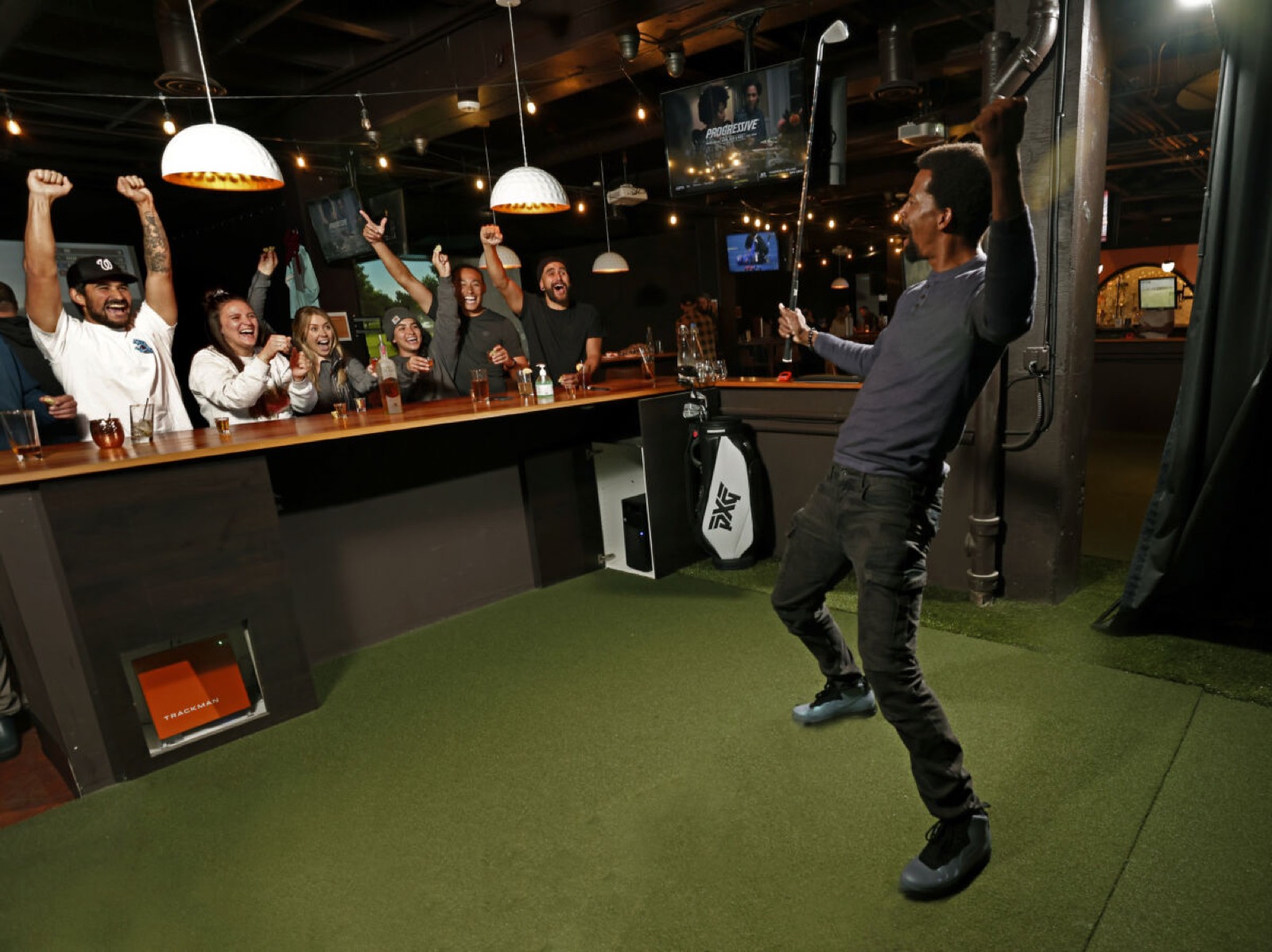 A golfer celebrating in a bay while a group cheers from the bar