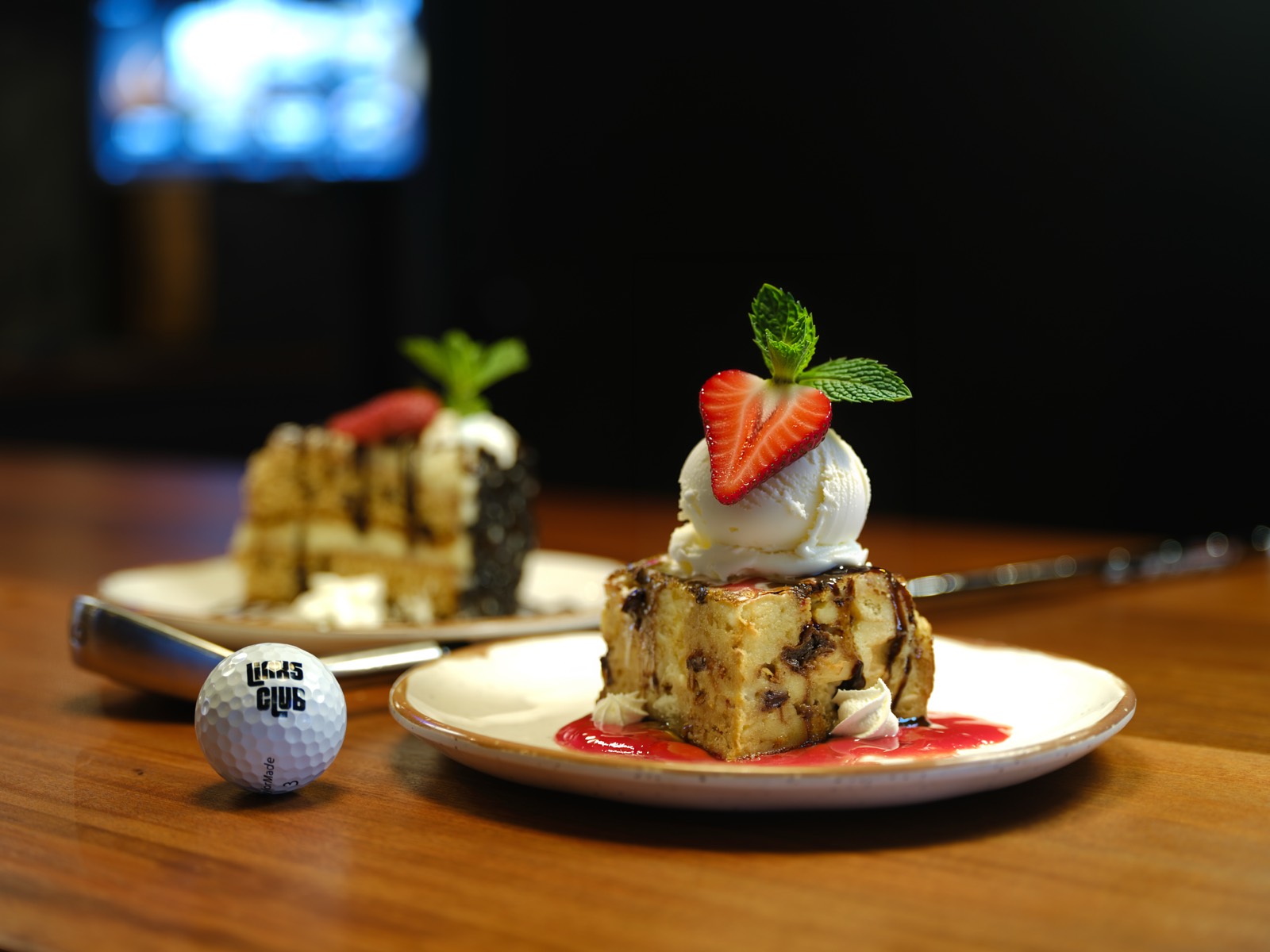 Warm bread pudding topped with vanilla ice cream and a strawberry, with layer cake behind