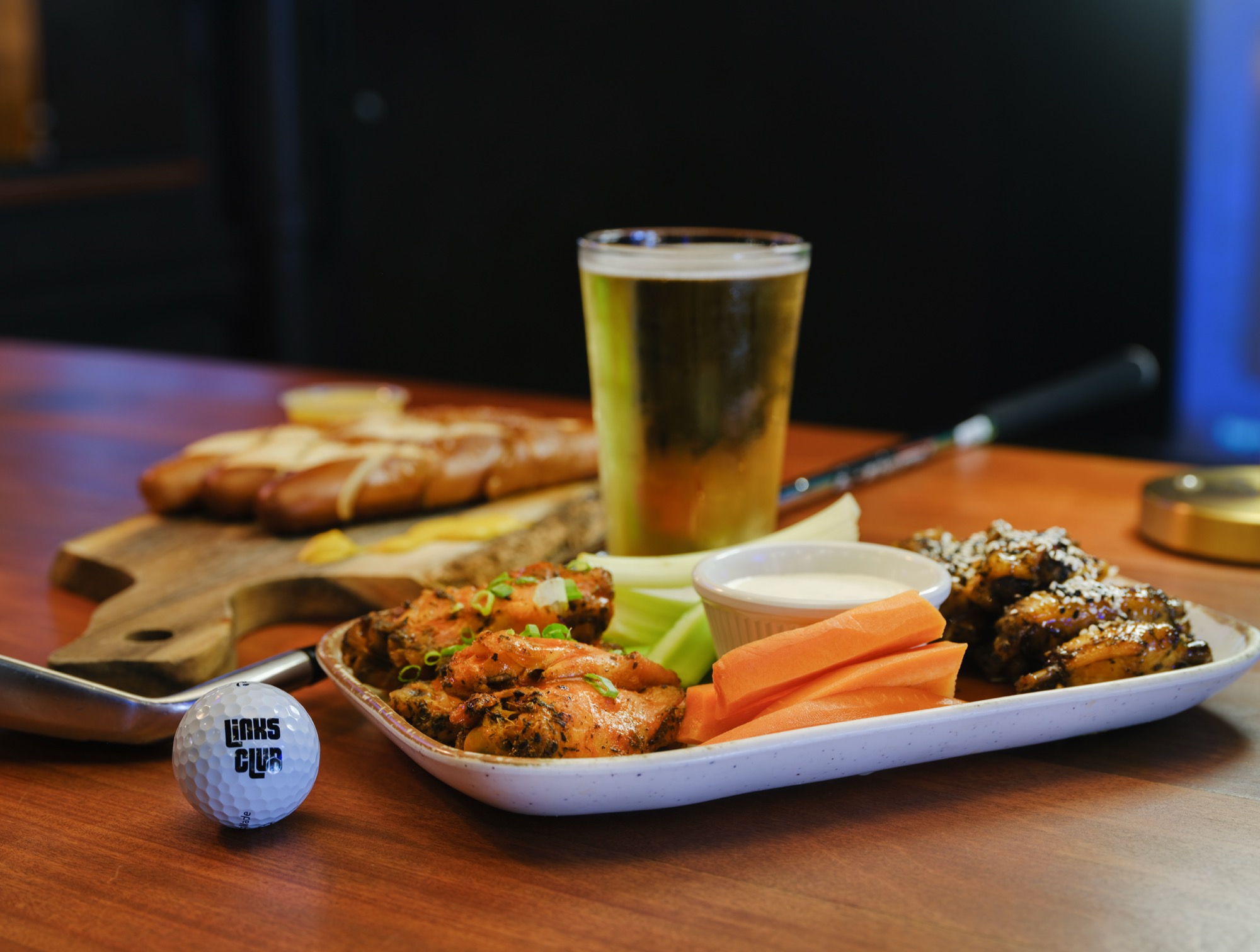 A platter of traditional and sesame wings with a cold beer, pretzel sticks, and a Links Club golf ball
