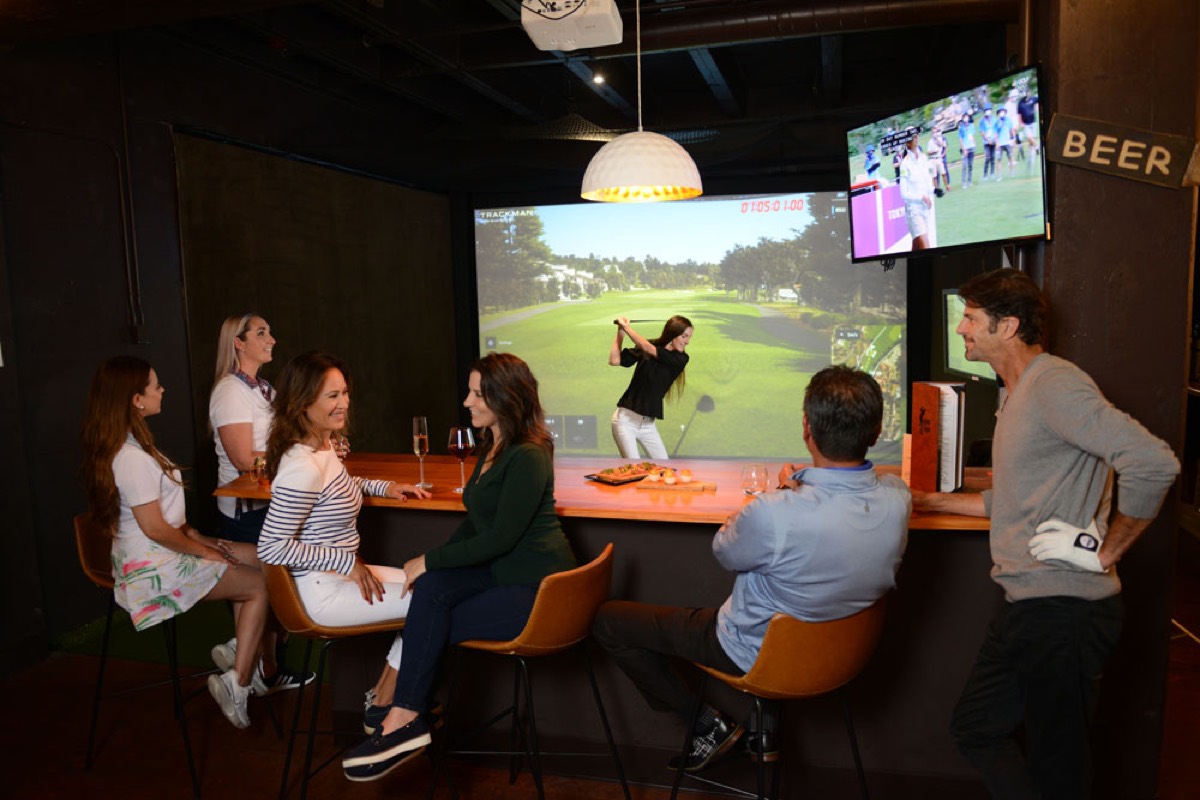 A golfer mid-swing in a Links Club simulator bay